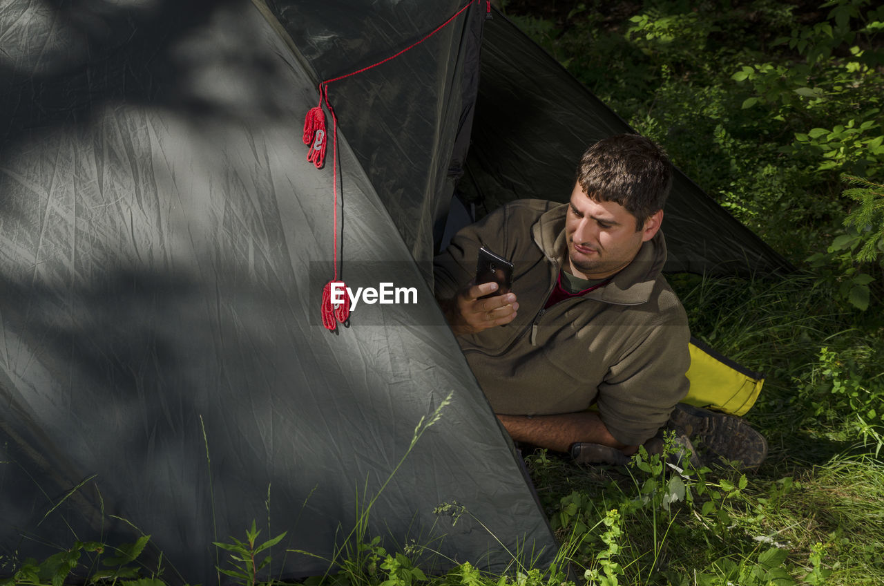 High angle view of man using phone while lying in tent