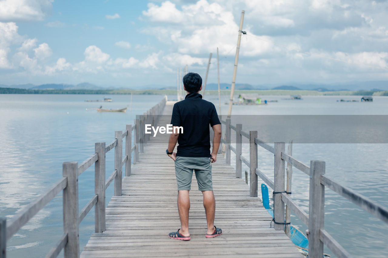 Rear view of man standing on pier in sea