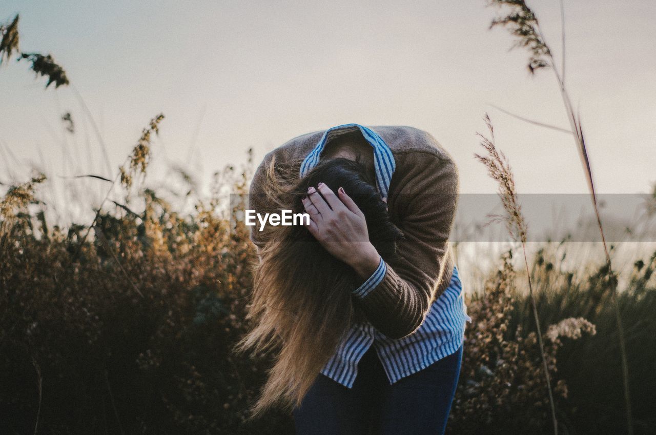 Woman with head in hand bending on field against clear sky