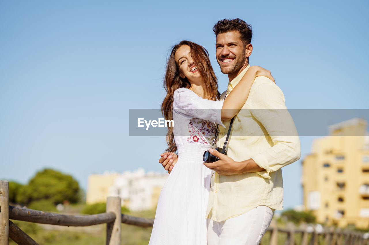 Smiling couple standing against clear blue sky during sunny day
