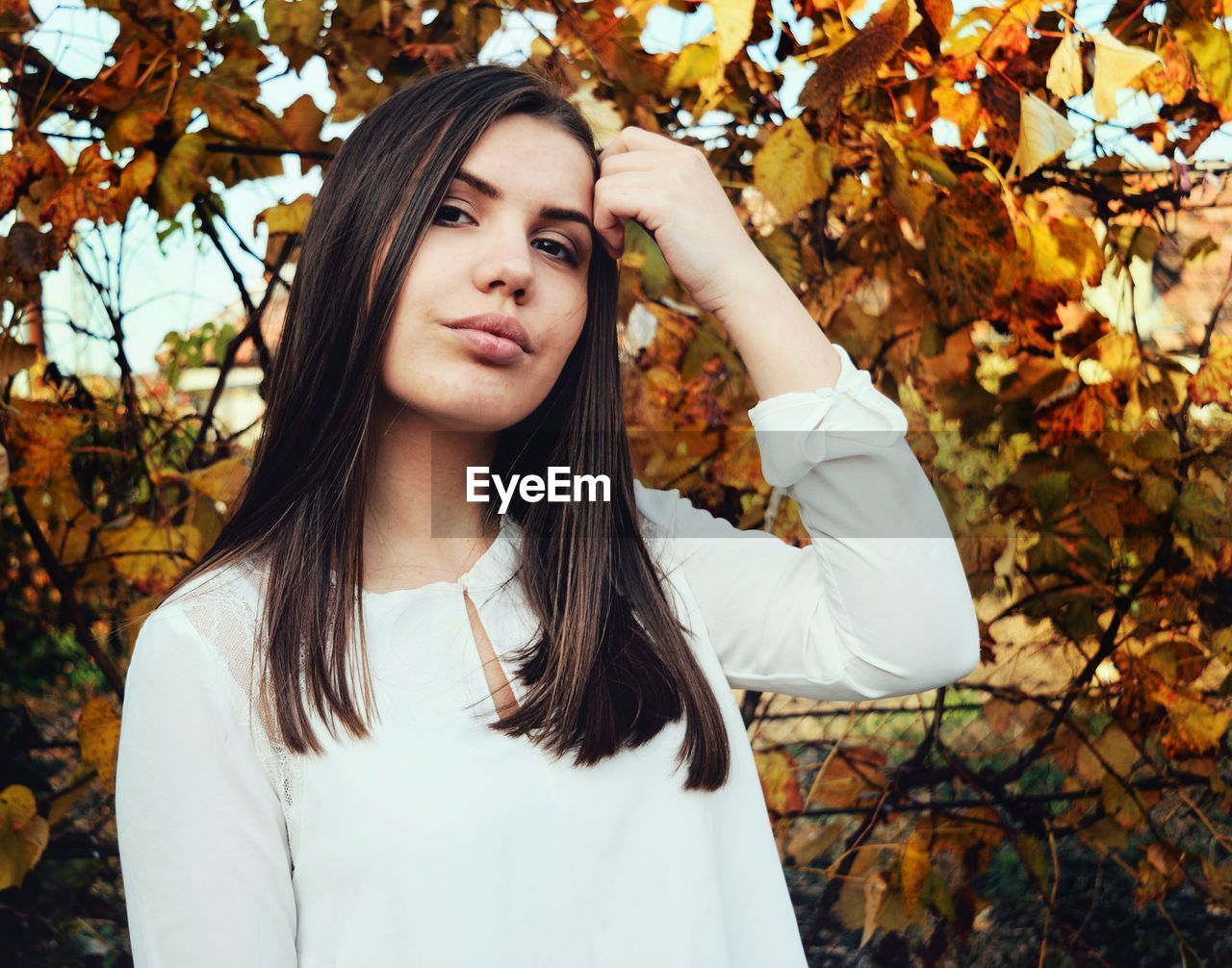 Portrait of beautiful young woman standing against autumn tree