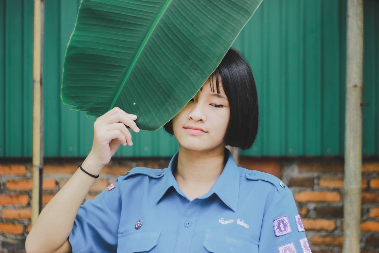 Young woman with leaf standing against brick wall