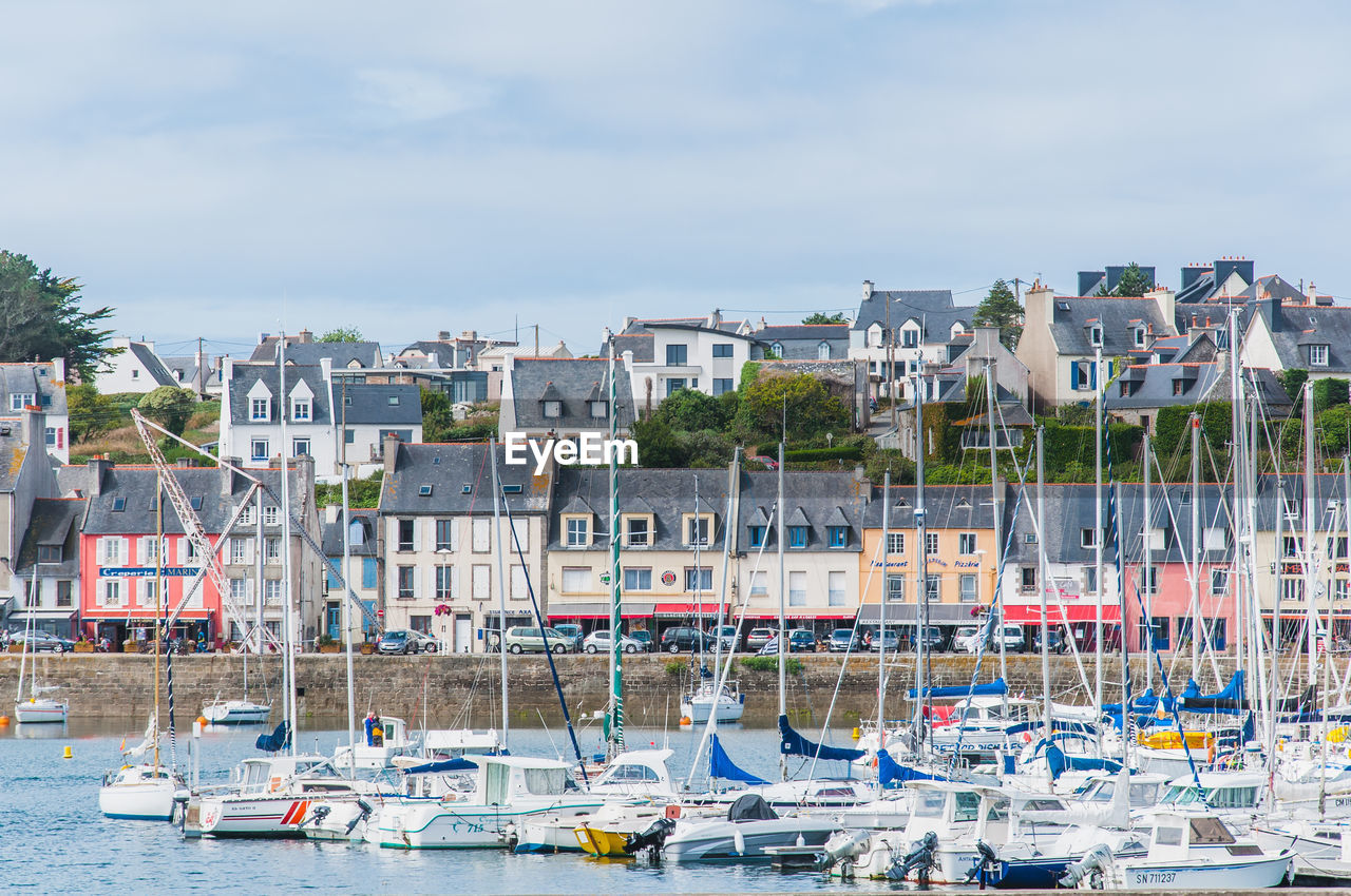 SAILBOATS MOORED IN HARBOR AGAINST BUILDINGS IN CITY