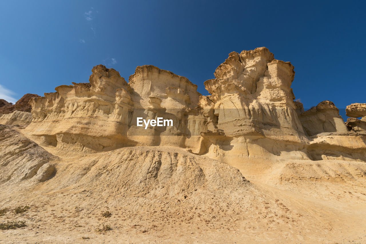 LOW ANGLE VIEW OF ROCK FORMATIONS AGAINST BLUE SKY