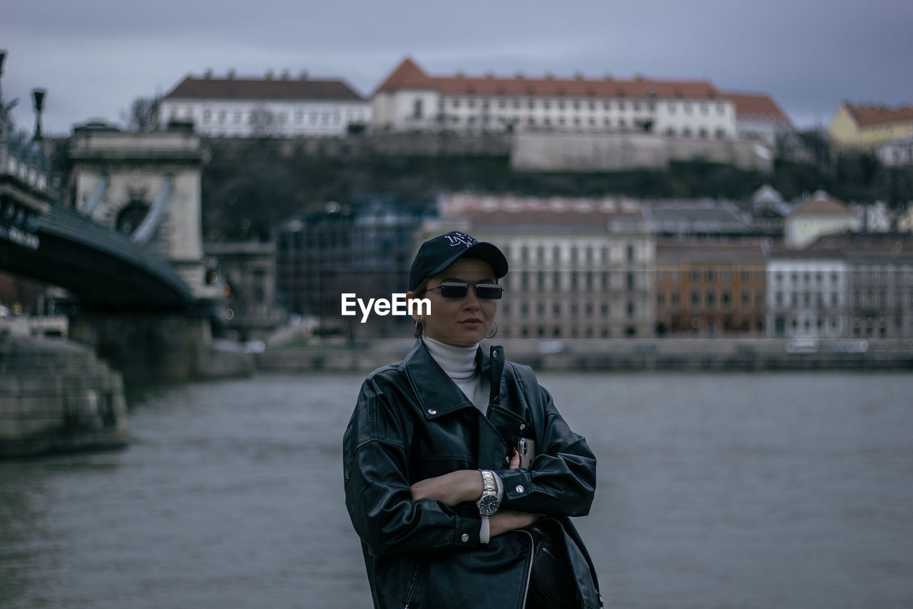 MAN WEARING SUNGLASSES STANDING ON BRIDGE OVER CANAL