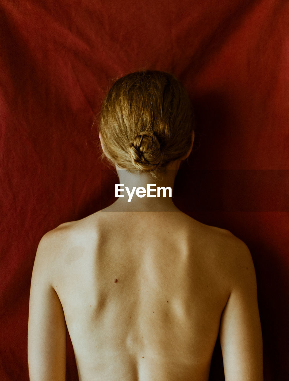 Rear view of shirtless young woman standing against red wall. uncertainty, love, mental health