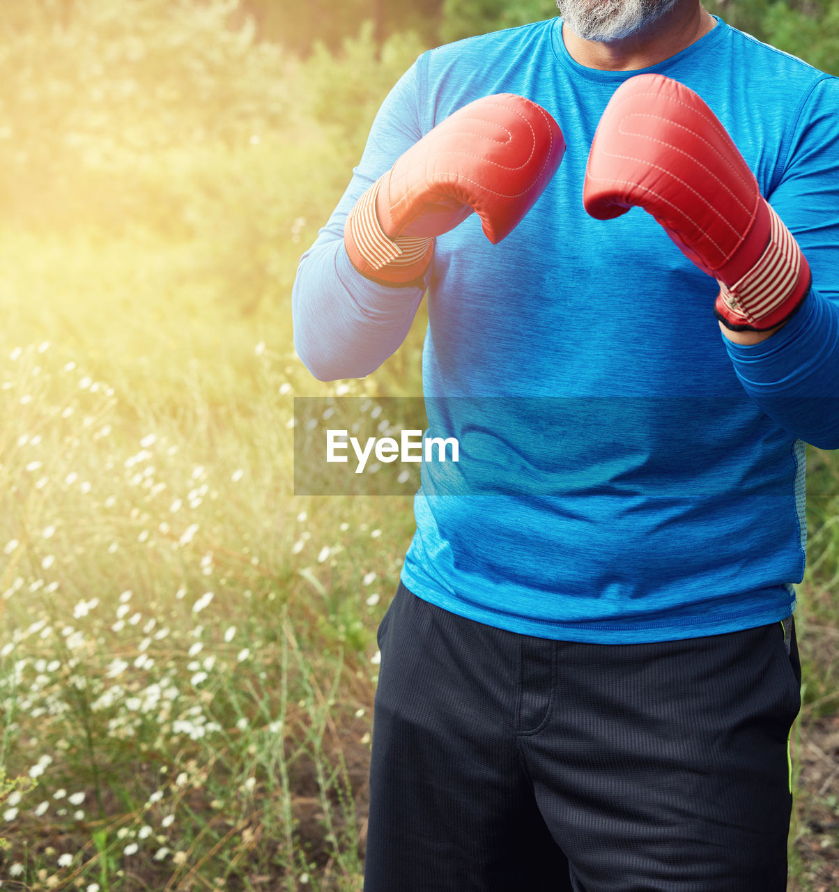 Midsection of man wearing boxing gloves while standing on field