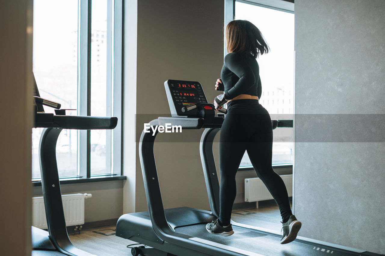 Young fitness brunette woman training for cardio equipment treadmill at gym