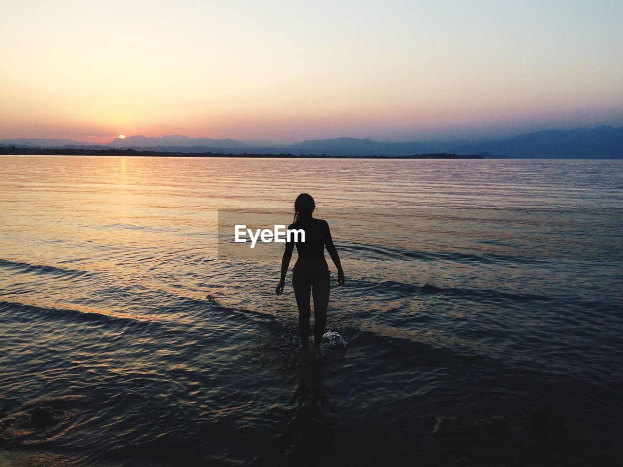 Silhouette woman standing at beach against sky during sunset