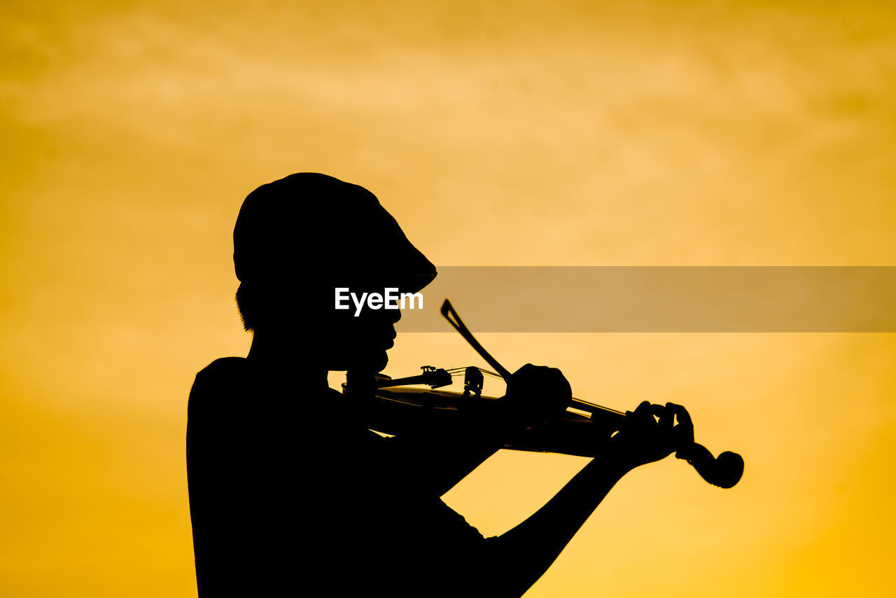 Silhouette boy playing violin against sky during sunset