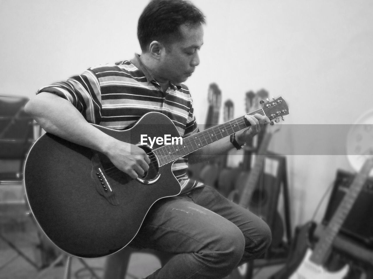 Mature man playing guitar while sitting on chair against wall