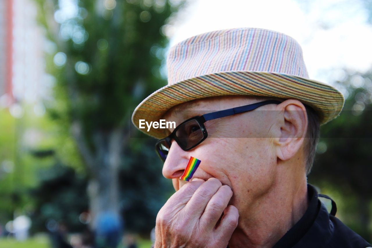 Close-up of woman in hat and sunglasses with small rainbow flag