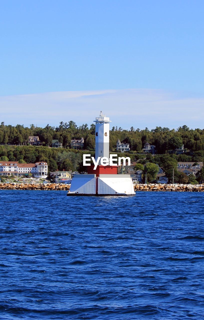 Lighthouse by sea against clear blue sky