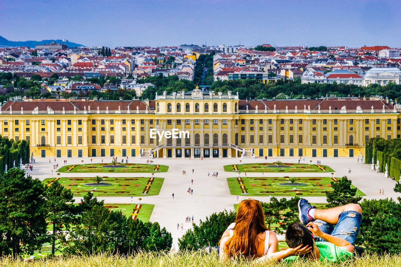 Rear view of couple lying on grass against buildings in city