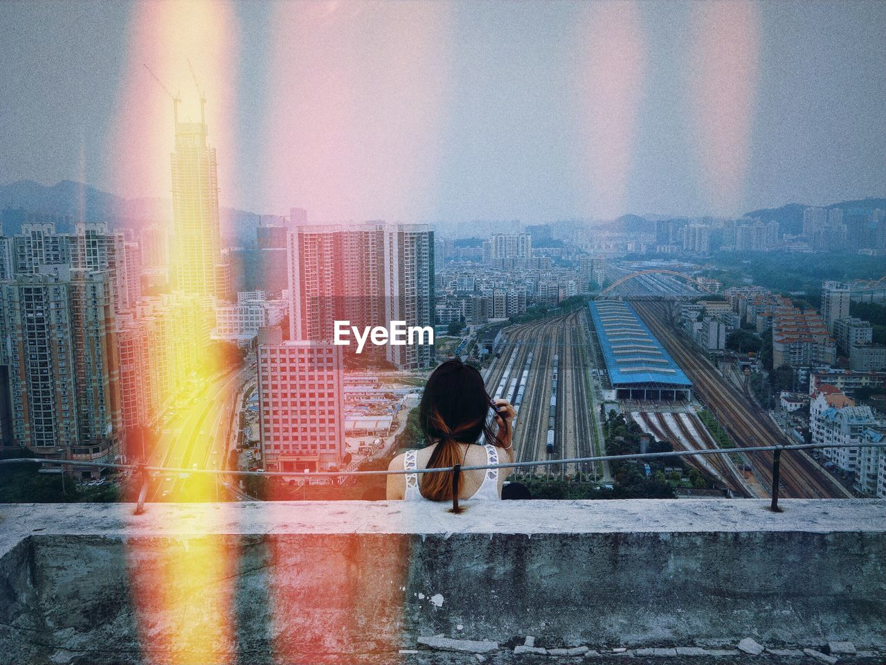 Rear view of woman sitting on rooftop against cityscape