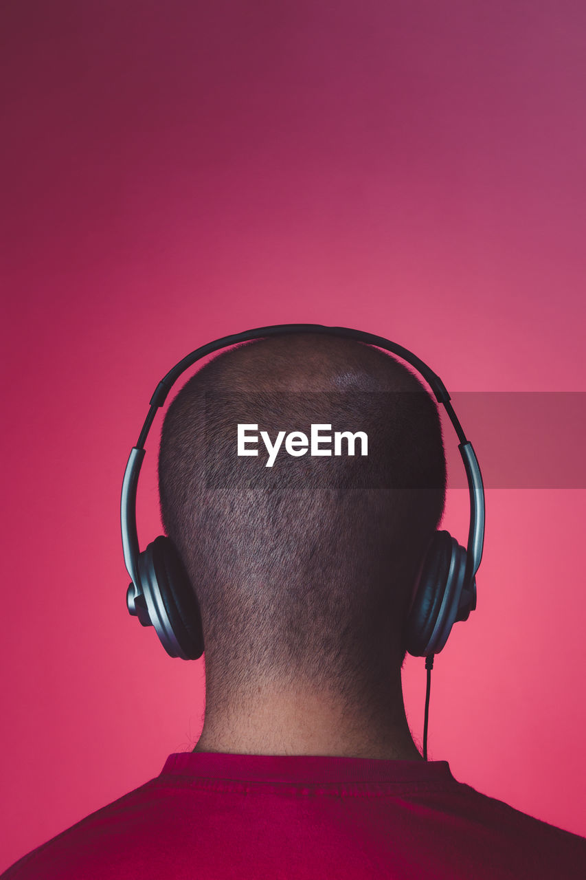 Rear view of man listening music against red background