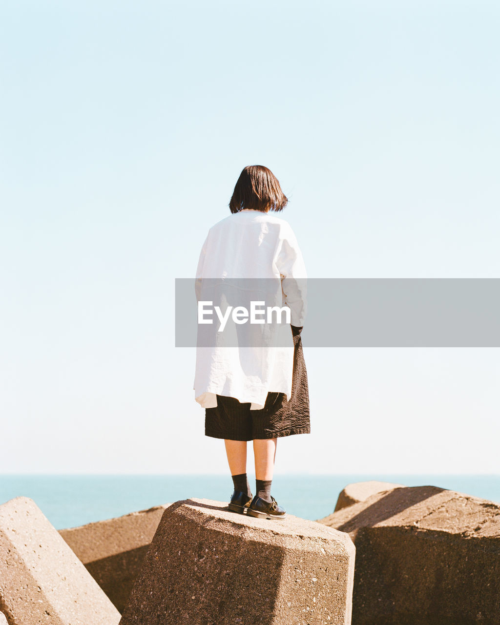 Rear view of woman standing on rocks by sea against clear sky