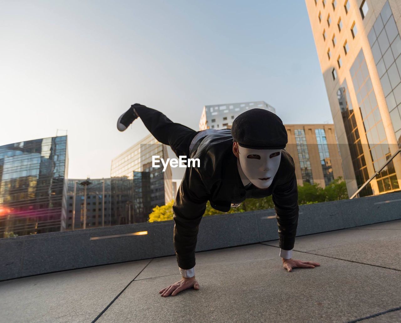 Man wearing mask doing handstand in city against clear sky