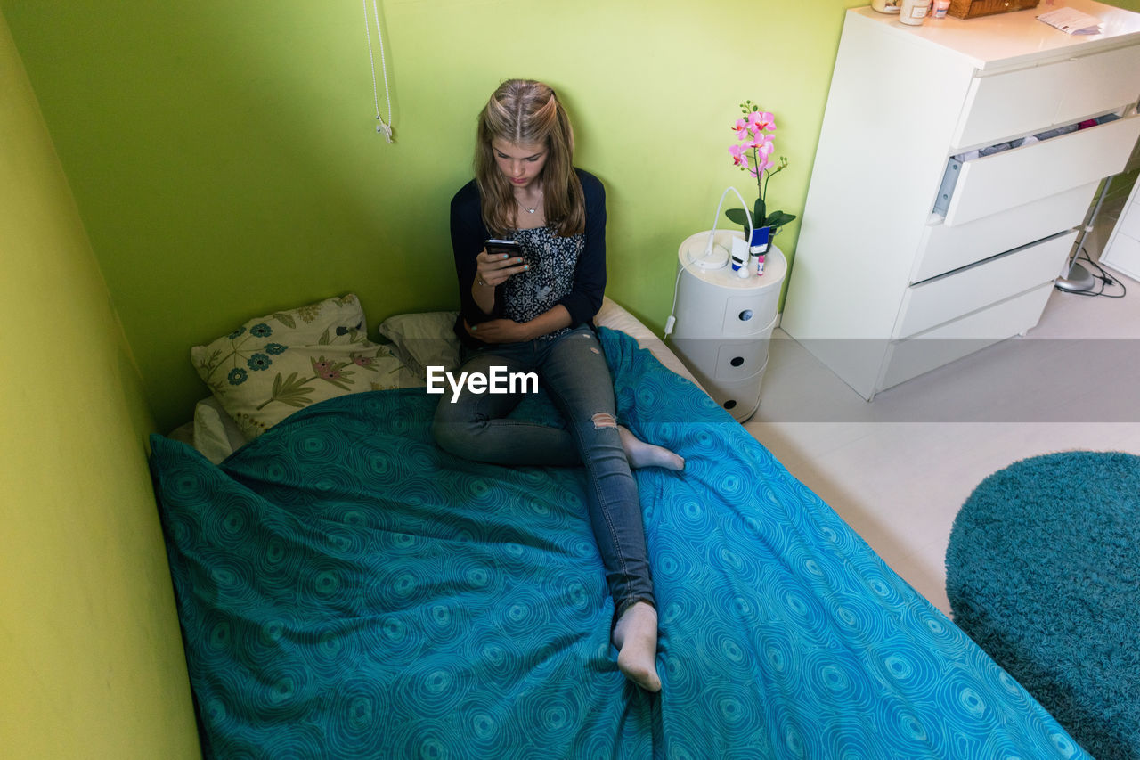 High angle view of teenage girl using smart phone while sitting on bed at home