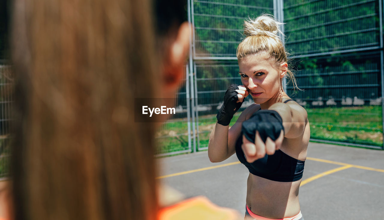 Portrait of female athlete exercising with friend on court against fence