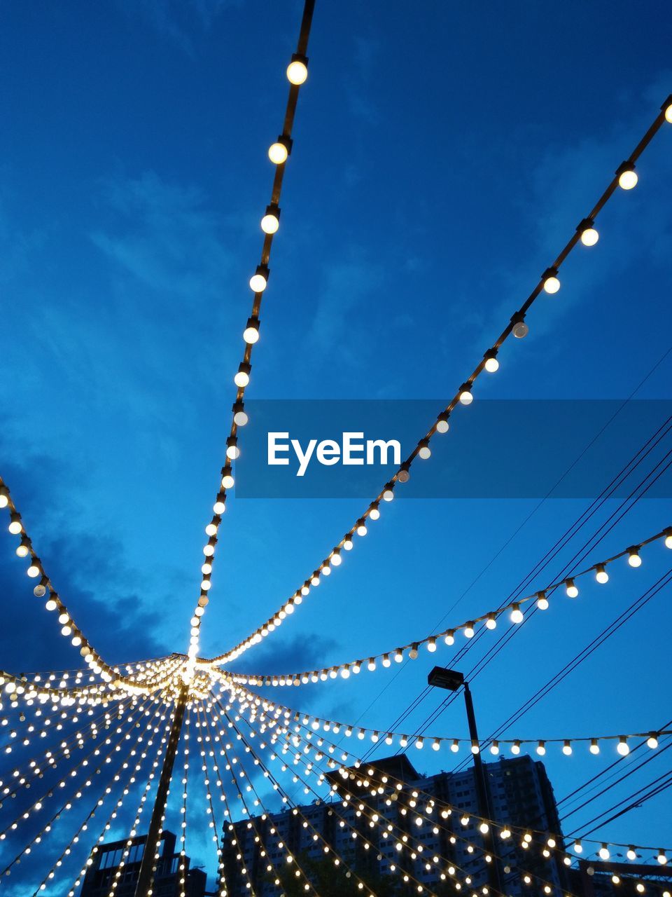 Low angle view of illuminated light bulbs against blue sky