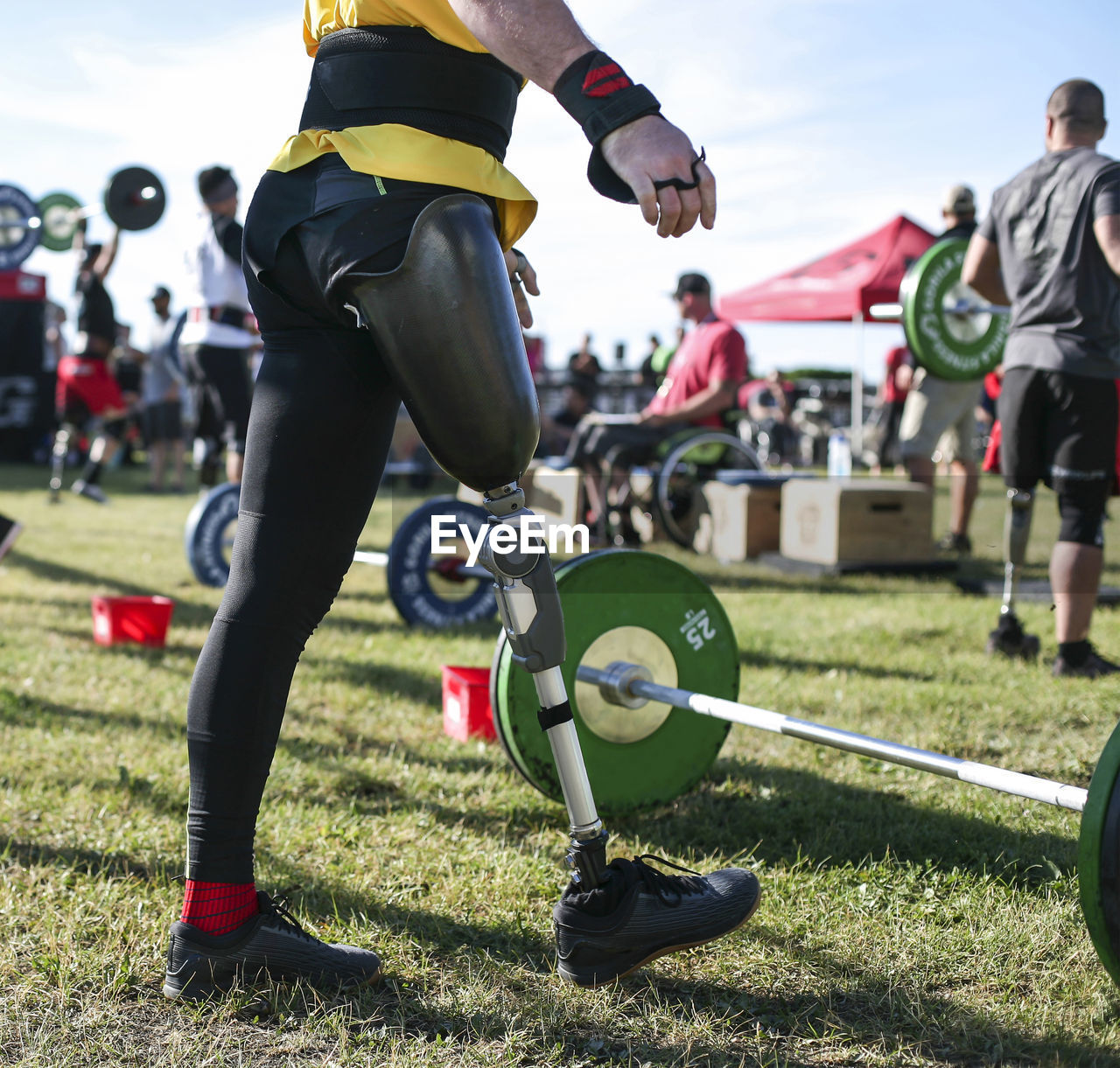 Low section of male adaptive athlete standing by deadlift on grassy field at park