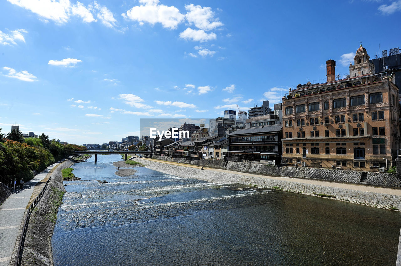 BRIDGE OVER RIVER AMIDST BUILDINGS AGAINST SKY
