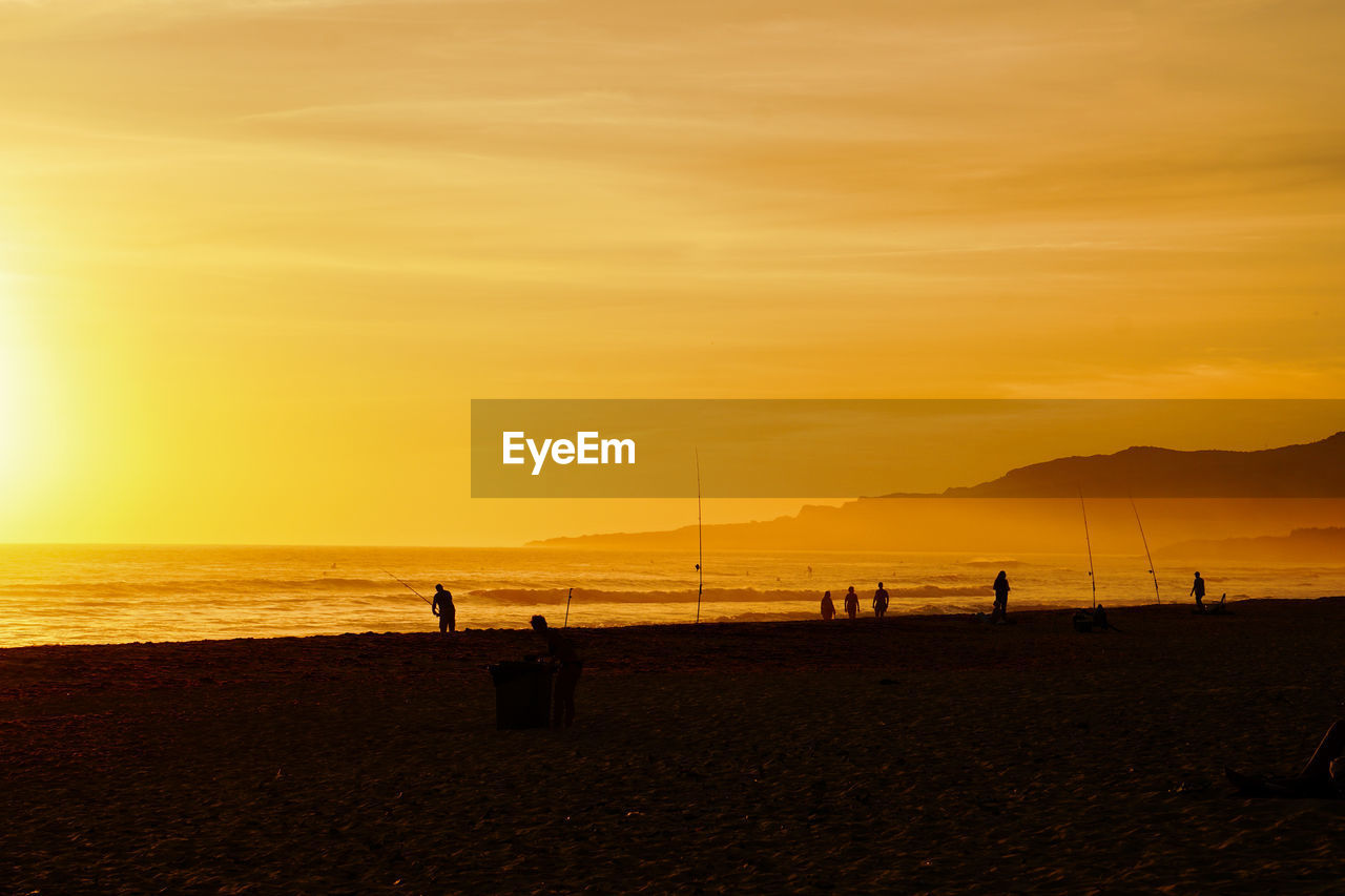 Silhouette people on beach against sky during sunset