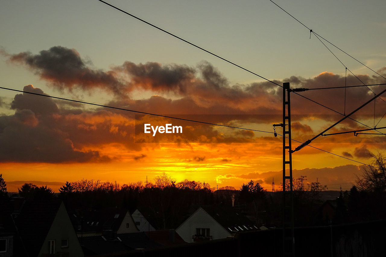 Houses by electricity pylon against orange cloudy sky