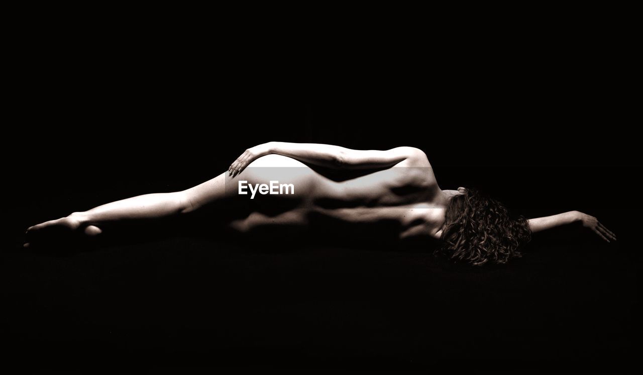 Rear view of naked woman lying over black background