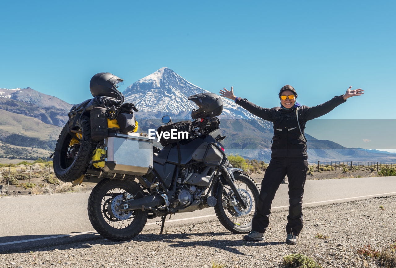 Woman standing next to touring motorbike. lanin volcano in the back