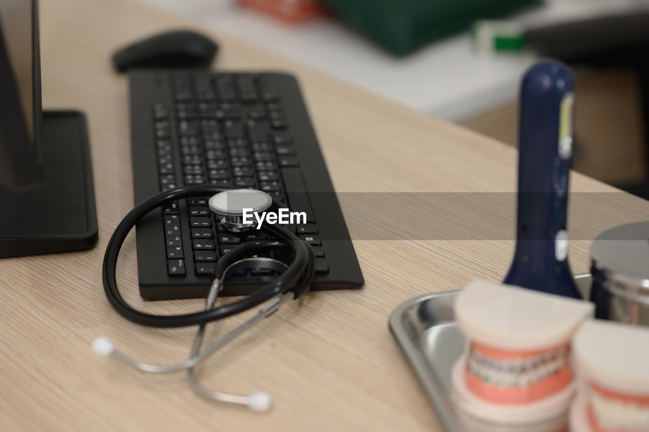 table, technology, computer, desk, indoors, furniture, communication, computer equipment, office, no people, wireless technology, business, keyboard, computer keyboard, computer mouse, wood, still life, selective focus, desktop pc, close-up, high angle view, cup, place of work