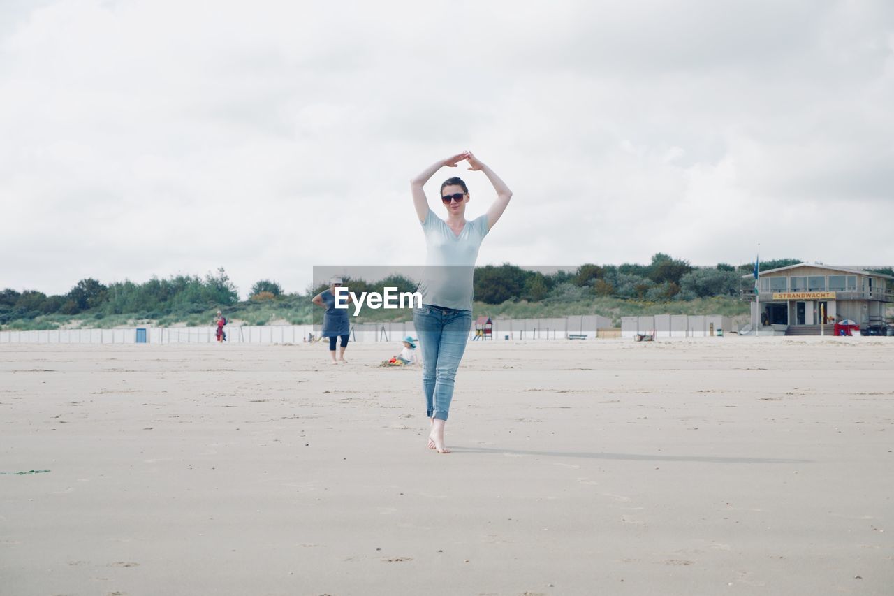 Full length of woman performing yoga at beach against sky