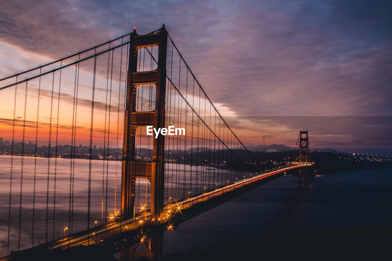 Golden gate bridge over river against cloudy sky during sunset