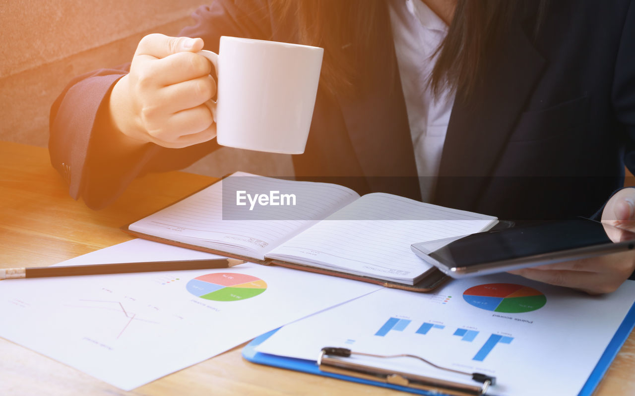 Midsection of businesswoman using digital tablet and holding coffee cup on desk