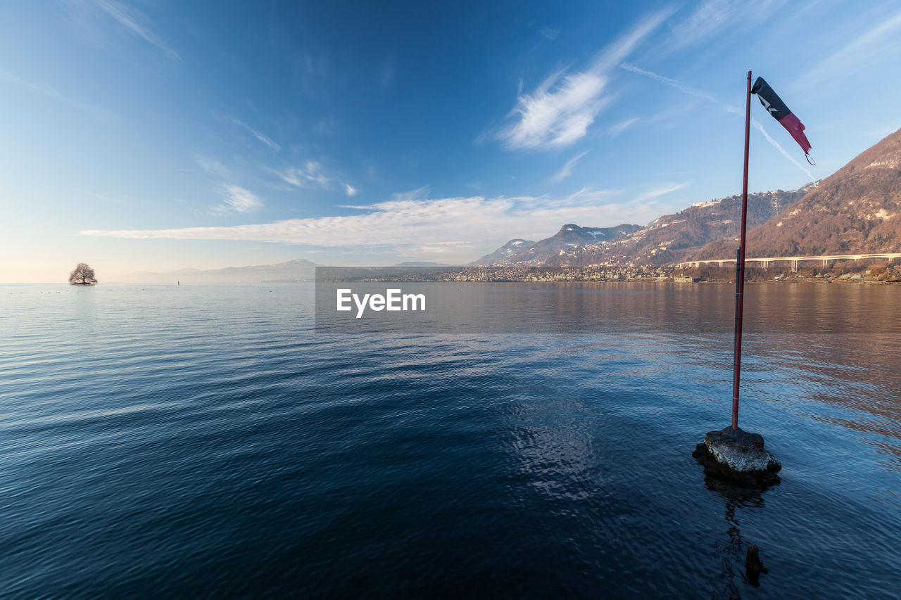 water, sky, sea, horizon, reflection, nature, flag, scenics - nature, ocean, beauty in nature, environment, blue, mountain, tranquility, no people, cloud, travel, travel destinations, tranquil scene, transportation, vehicle, landscape, dusk, land, outdoors, coast, nautical vessel, patriotism, pole, bay, sunlight, architecture, day, body of water, mountain range, shore, sailing, mode of transportation, wave, idyllic, beach