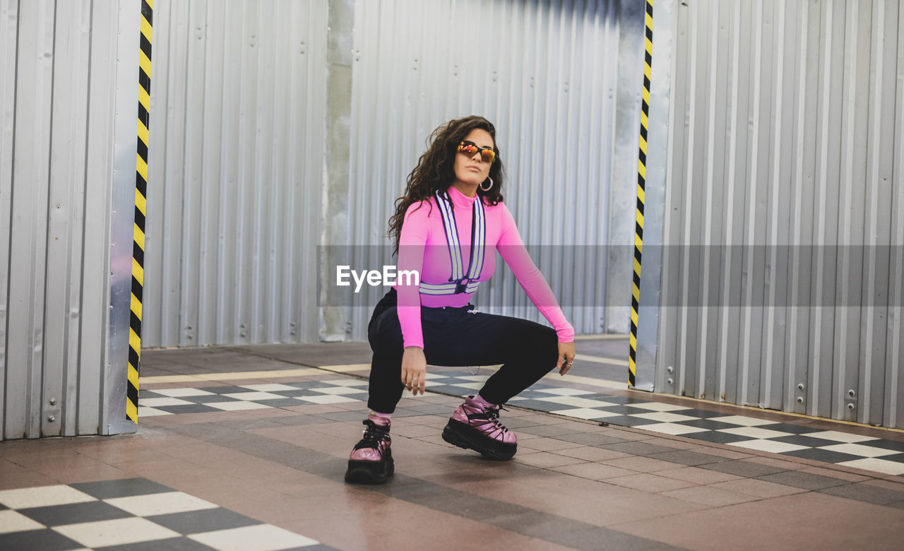 Full length portrait of woman crouching against corrugated iron