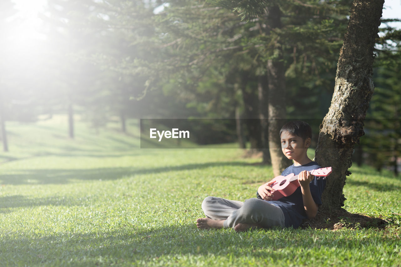 Boy playing guitar while sitting on grassy field at park