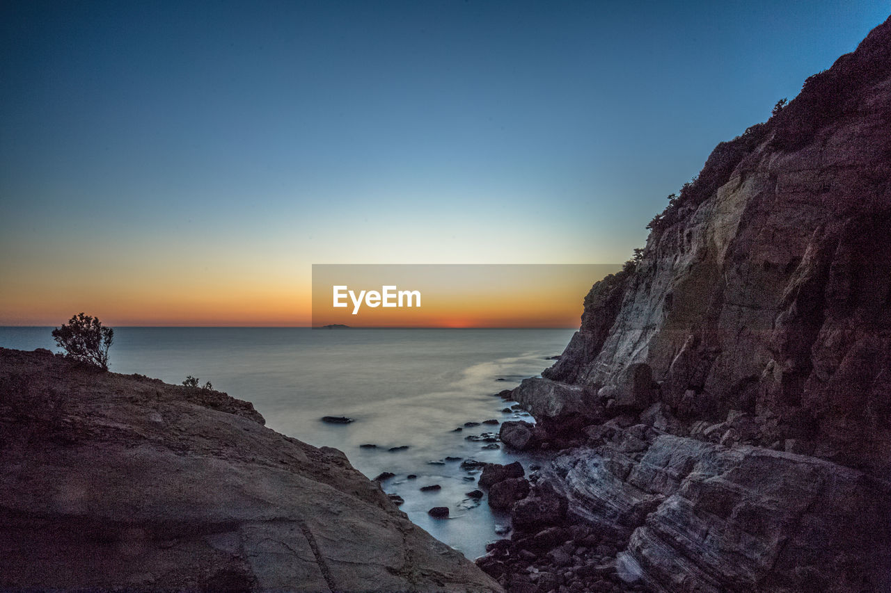 Rock formation on beach against sky during sunset