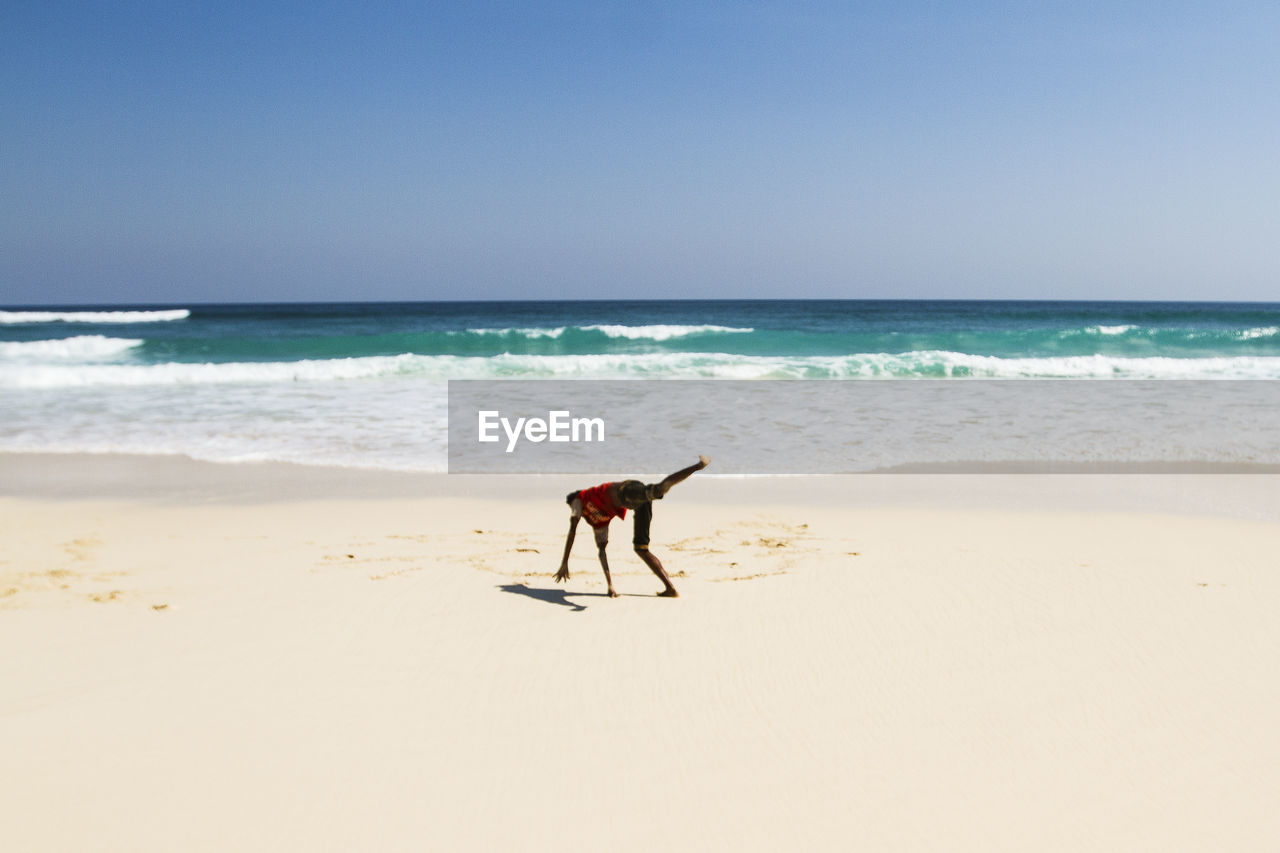 Man doing stunt at beach against clear blue sky