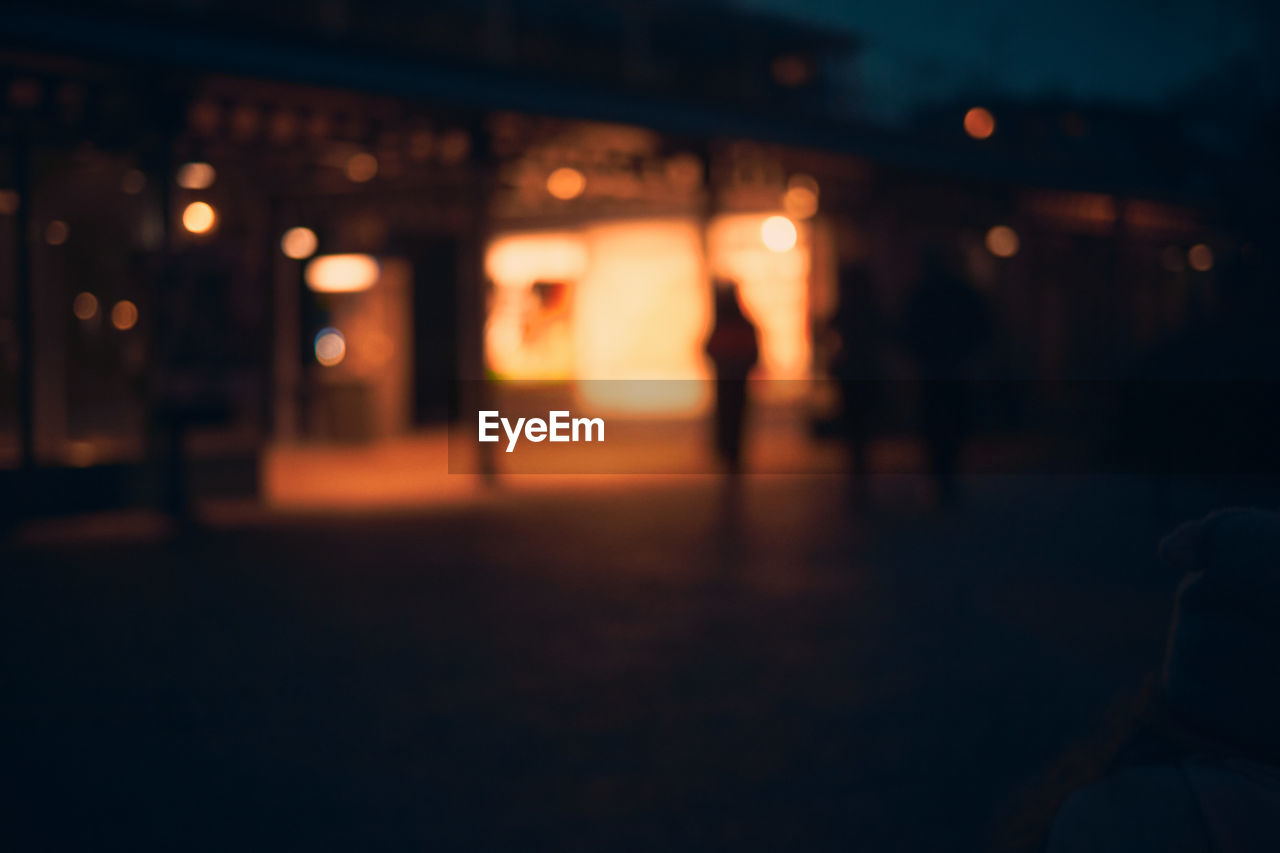 Defocused image of silhouette people on illuminated street at night