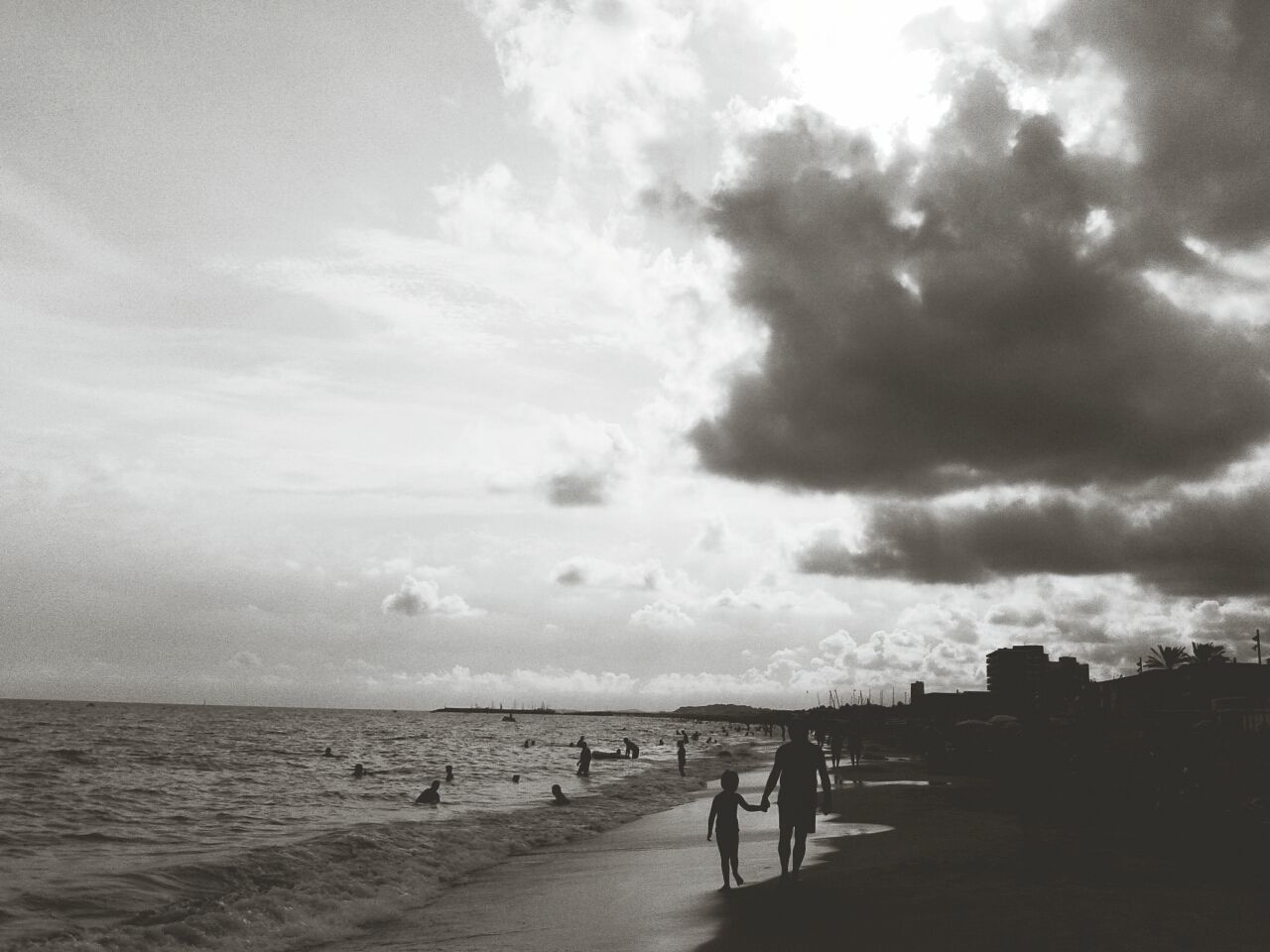 Silhouette people at beach against cloudy sky
