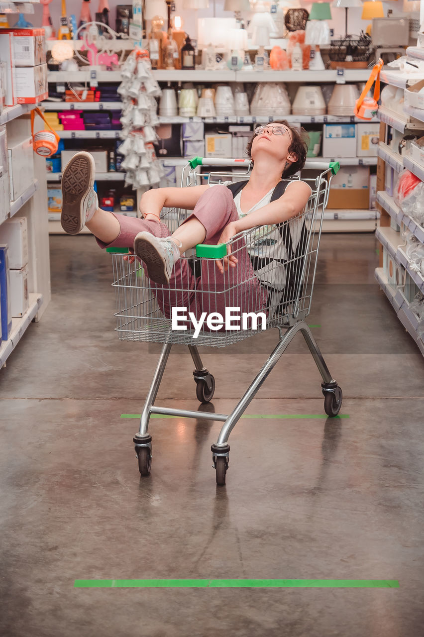 The girl is sitting in a basket in the trading floor. a lady rides in a cart in an empty store