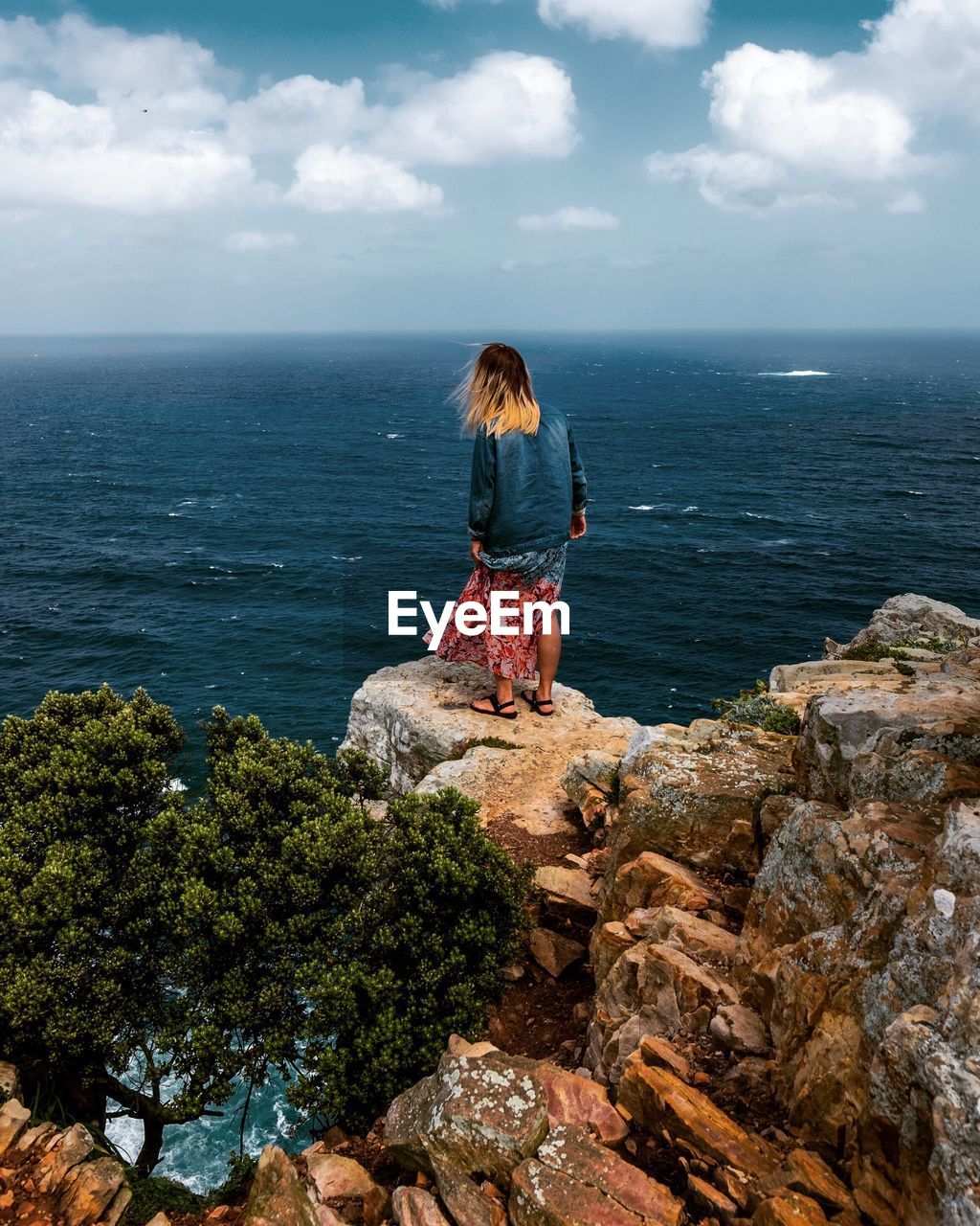 Rear view of woman standing on rock against sea