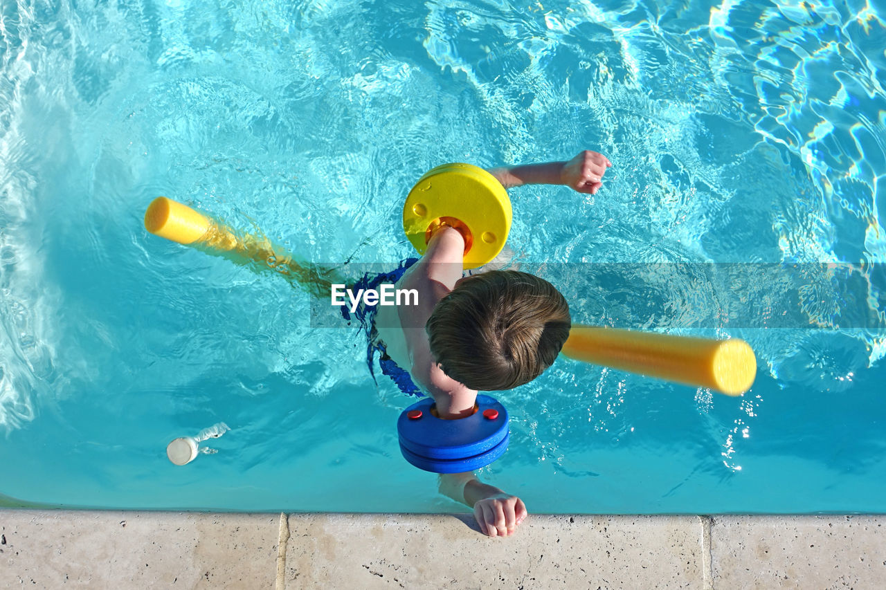 Top view of little boy floating in swimming pool with floats and arm bands