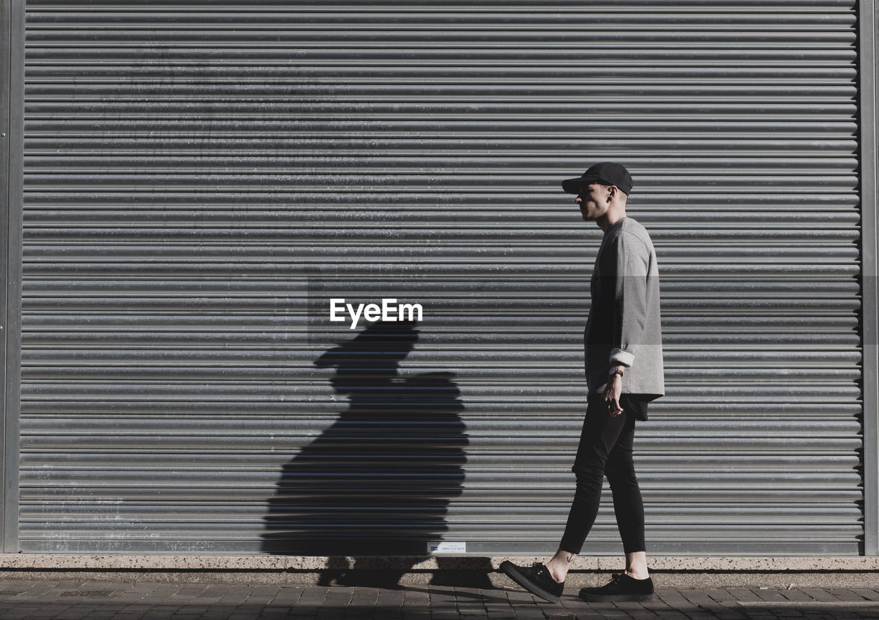 Side view of man walking against closed shutter