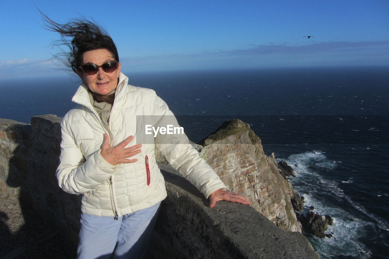 Woman wearing sunglasses standing on cliff by sea