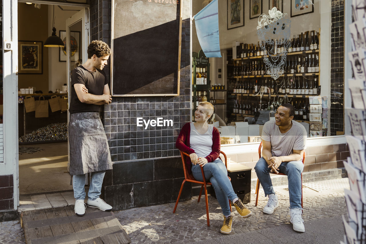 Customers talking to male owner standing by store doorway