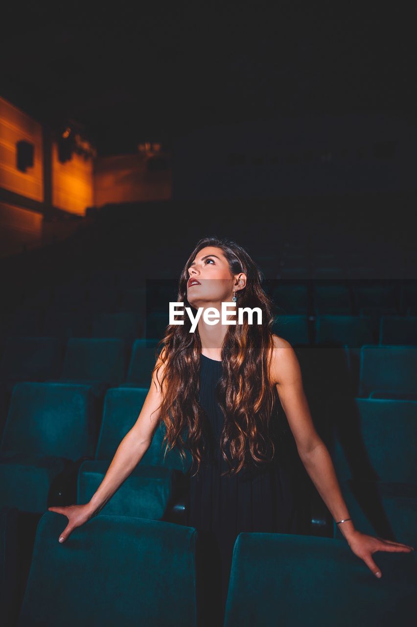 Beautiful young woman looking away while standing in movie theater