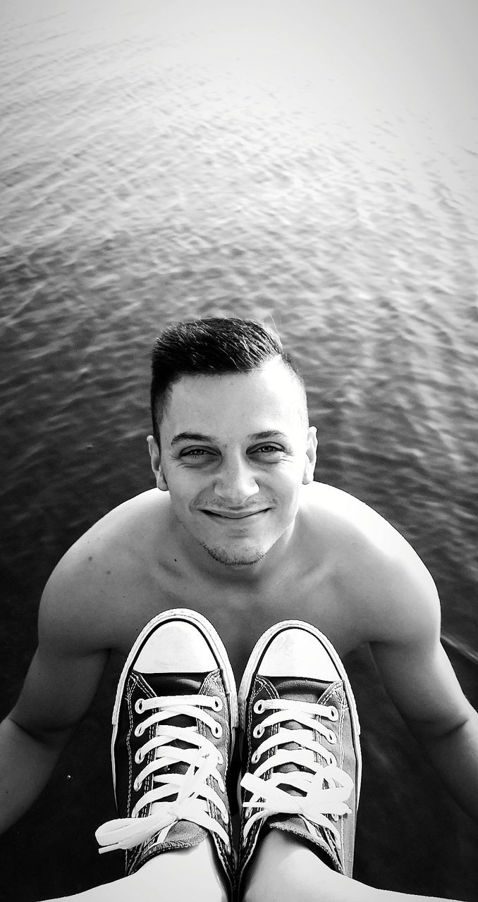 Portrait of smiling young man standing by legs in lake